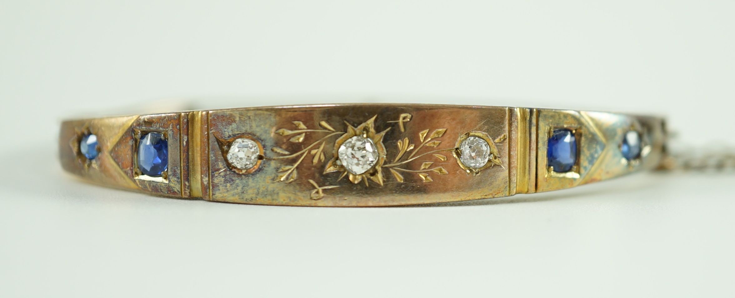 A late Victorian engraved gold, gypsy set three stone diamond and four stone sapphire set hinged bangle